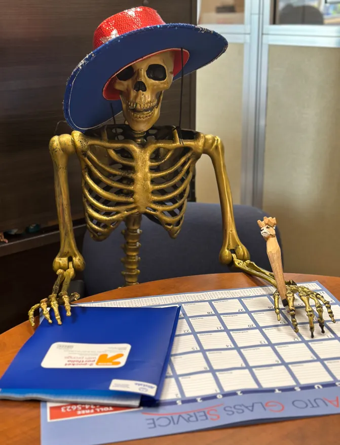 A skeleton wearing a wide-brimmed cowboy hat seated at an office desk with a calendar